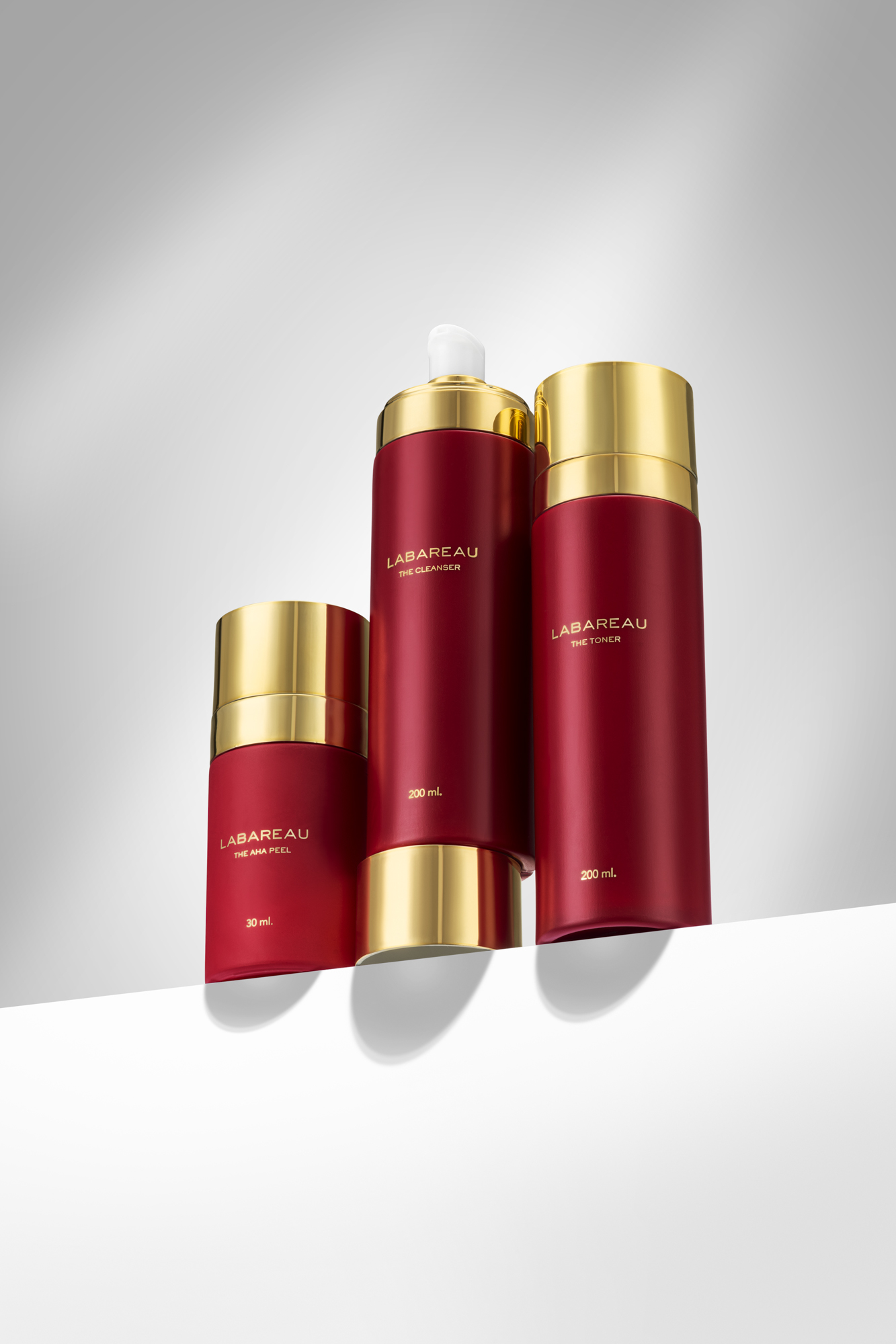 High-end cosmetica productfotografie van Labareau cleanser, toner en AHA peel in luxe rood-gouden verpakking.