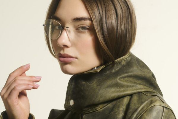 Close-up eyewear fotografie van vrouwelijk model met randloze bril en groene leren jas in professionele fotostudio.