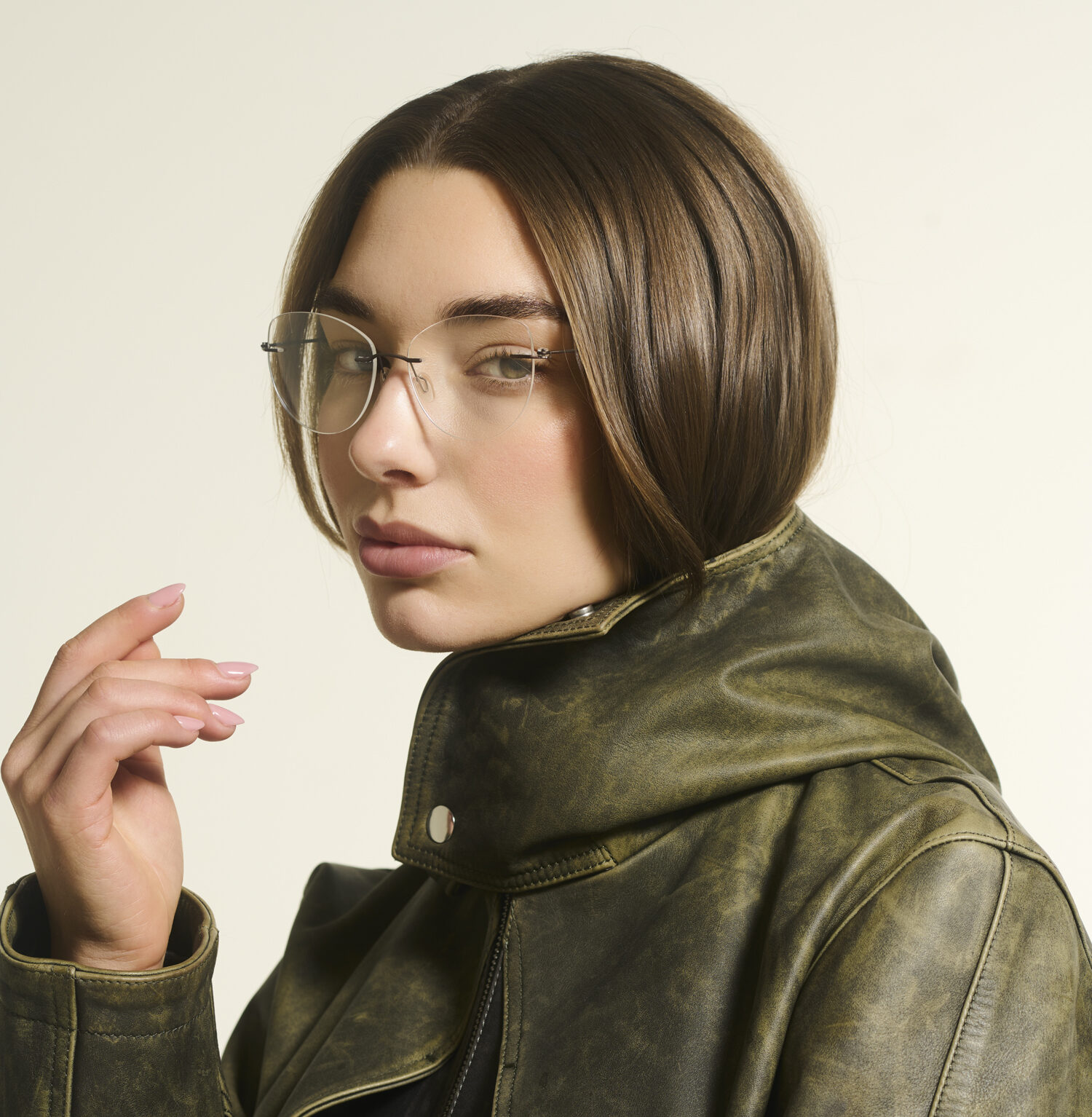 Close-up eyewear fotografie van vrouwelijk model met randloze bril en groene leren jas in professionele fotostudio.