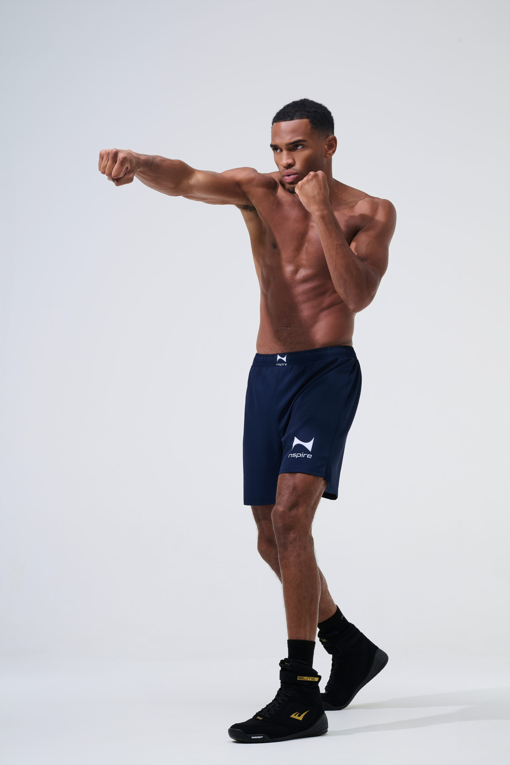 Dynamische sportfotografie van mannelijk model in donkerblauwe Nspire trainingsshort tijdens een bokspose in studio.