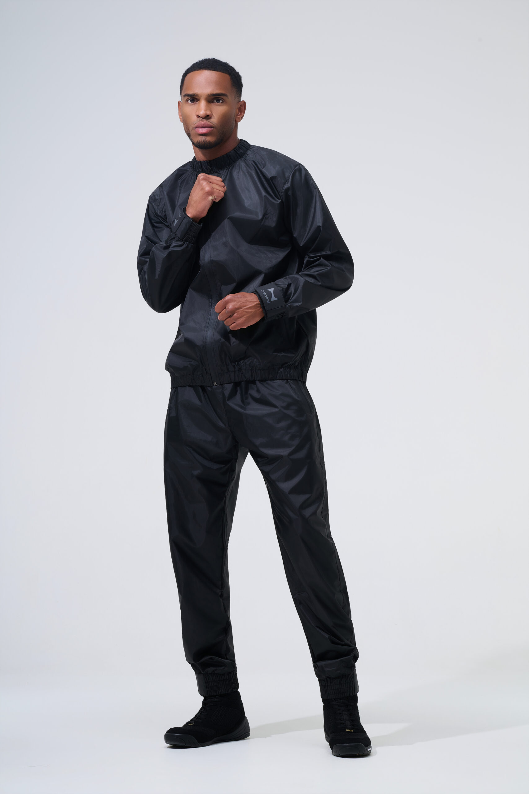 Professionele sportkleding fotografie van mannelijk model in zwarte Nspire trainingsset op lichte studioachtergrond.