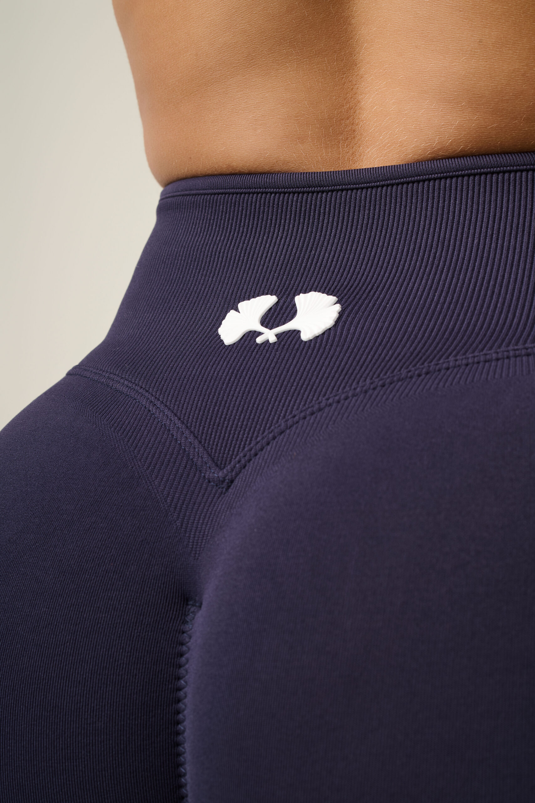 Close-up productfotografie van donkerpaarse sportlegging met hoge taille, logo en zichtbare stofstructuur.