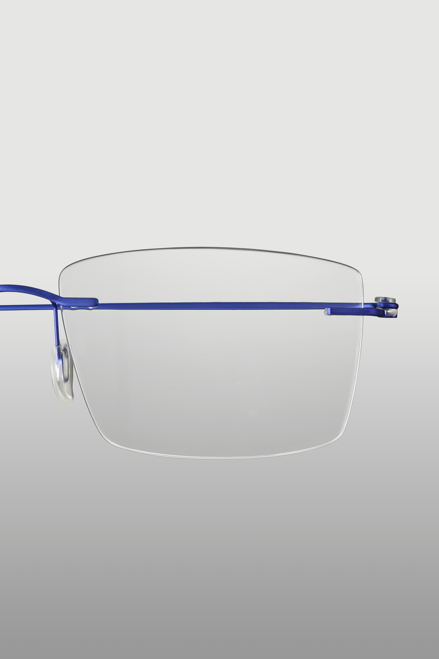 Professionele productfotografie van blauwe randloze bril met transparant glas op lichtgrijze achtergrond.