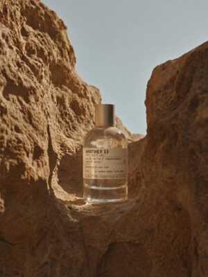 Parfumfles Another 13 van Le Labo, sfeervol gefotografeerd tussen zandkleurige rotsformaties in warm, natuurlijk licht.