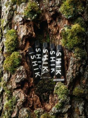 Vijf zwarte tubes van HIK skincare, geplaatst in een boomstam en omringd door groene mossen en ruwe boomschors.